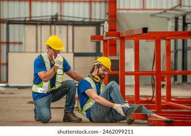 A worker wearing a hard hat and safety vest is injured and holding his leg while another worker wearing a hard hat and safety vest kneels beside him and holds his arm. - Powered by Shutterstock