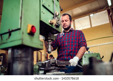 Worker wearing plaid shirt using drill press in factory - Powered by Shutterstock