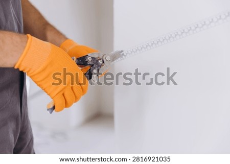 Worker wearing protective gloves using snips to cut a metal corner bead for plasterboard installation during home renovation