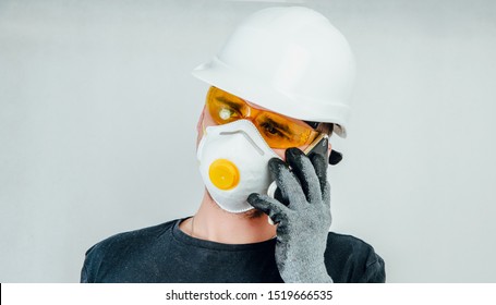 A worker wearing a protective helmet, face mask and safety glasses is talking on a mobile phone. Work concept, hiring workers for construction. Appropriate Preparation for work, safety.