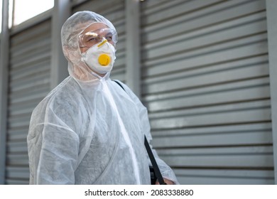 Worker Wearing Protective Suit Disinfection Gear Disinfect Surface Public Place Parking. Side View Of Disinfector Safety Overall And Respiratory Mask Covid Pandemic Disinfection Preventive Measures