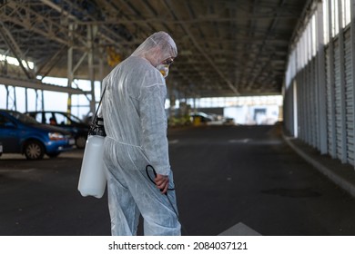 Worker Wearing Protective Suit Disinfection Gear Disinfect Surface Public Place Parking. Side View Of Disinfector Safety Overall And Respiratory Mask Covid Pandemic Disinfection Preventive Measures