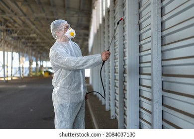 Worker Wearing Protective Suit Disinfection Gear Disinfect Surface Public Place Parking. Side View Of Disinfector Safety Overall And Respiratory Mask Covid Pandemic Disinfection Preventive Measures