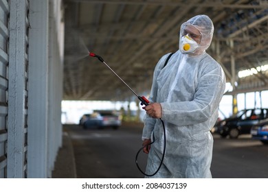 Worker Wearing Protective Suit Disinfection Gear Disinfect Surface Public Place Parking. Side View Of Disinfector Safety Overall And Respiratory Mask Covid Pandemic Disinfection Preventive Measures