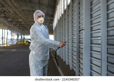 Worker Wearing Protective Suit Disinfection Gear Disinfect Surface Public Place Parking. Side View Of Disinfector Safety Overall And Respiratory Mask Covid Pandemic Disinfection Preventive Measures