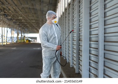 Worker Wearing Protective Suit Disinfection Gear Disinfect Surface Public Place Parking. Side View Of Disinfector Safety Overall And Respiratory Mask Covid Pandemic Disinfection Preventive Measures