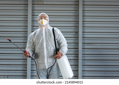 Worker Wearing Protective Suit Disinfection Gear Disinfect Surface Public Place Parking. Side View Of Disinfector Safety Overall And Respiratory Mask Covid Pandemic Disinfection Preventive Measures