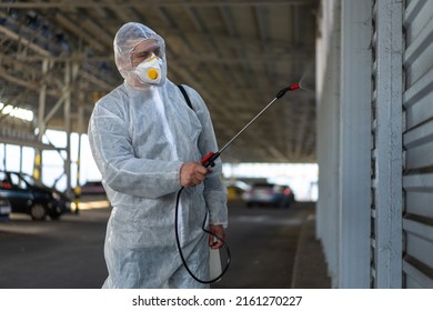 Worker Wearing Protective Suit Disinfection Gear Disinfect Surface Public Place Parking. Side View Of Disinfector Safety Overall And Respiratory Mask Covid Pandemic Disinfection Preventive Measures