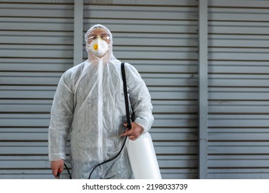 Worker Wearing Protective Suit Disinfection Gear Disinfect Surface Public Place Parking. Side View Of Disinfector Safety Overall And Respiratory Mask Covid Pandemic Disinfection Preventive Measures