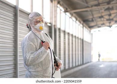 Worker Wearing Protective Suit Disinfection Gear Disinfect Surface Public Place Parking. Side View Of Disinfector Safety Overall And Respiratory Mask Covid Pandemic Disinfection Preventive Measures