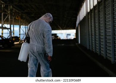 Worker Wearing Protective Suit Disinfection Gear Disinfect Surface Public Place Parking. Side View Of Disinfector Safety Overall And Respiratory Mask Covid Pandemic Disinfection Preventive Measures