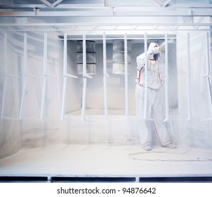Worker wearing protective wear performing powder coating of metal details in a special industrial camera