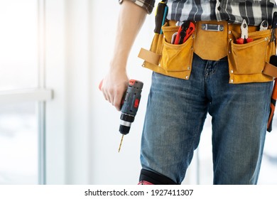 Worker wearing tool belt and holding mobile drill at home - Shutterstock ID 1927411307