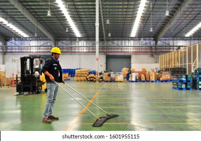 Worker wearing yellow safety helmet and holding a mop cleaning floor warehouse. - Powered by Shutterstock