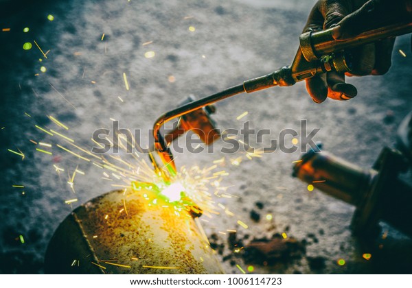 Worker welding\
joint steel exhaust pipe of\
car.