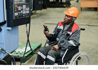 Worker in wheelchair operating industrial machine, wearing orange safety helmet and protective gear, ensuring safety and efficiency in factory environment - Powered by Shutterstock