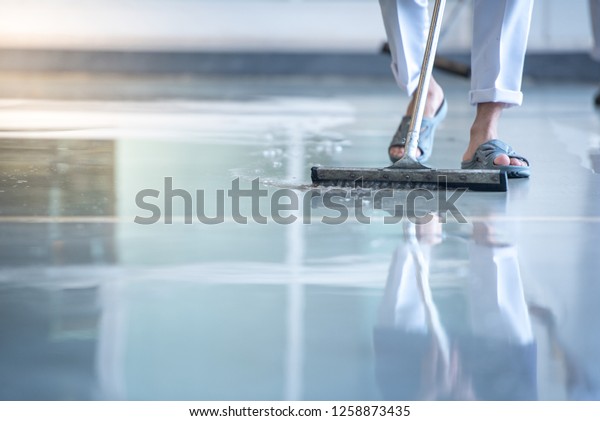 worker in White\
dress, protective uniform cleaning new epoxy floor in empty\
storehouse or car service\
center
