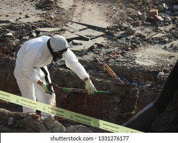 Worker with white protective suit, gloves and mask removes removal white asbestos on construction site. Demolition building, barrier tape  warning, caution hazard. Action picture, part of a serie.  
