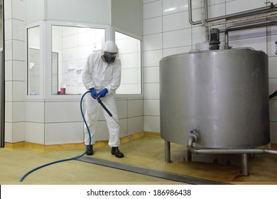 worker in white protective uniform,mask,gloves  with high pressure washer at  large industrial process tank  cleaning floor  in plant
