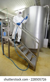 worker in white protective uniform,mask,gloves with high pressure washer on stairs at large industrial process tank preparing to cleaning