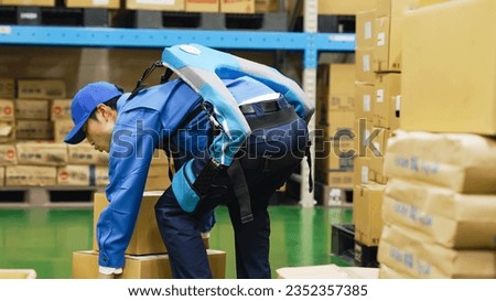 A worker who uses a power assist suit to carry packages in a warehouse.