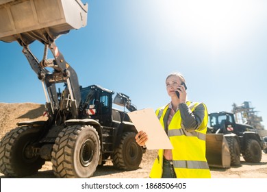 Worker woman with phone and clipboard in mine or quarry doing her job