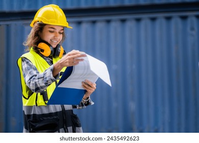 A worker woman wearing a yellow vest and a hard hat is reading a blue folder. She is smiling and she is happy - Powered by Shutterstock