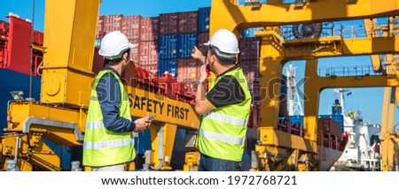 worker working with radio transceiver for controlling crane to loading container box to container ship in port shipping containers. logistics, sea transportation and logistics business concept