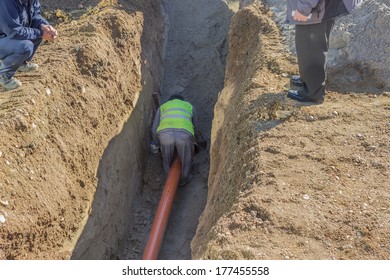 Worker Working In Trench. No Ladder, No Hardhat, Not Working In The Trench Box. Dangers Of Trench Collapse. 