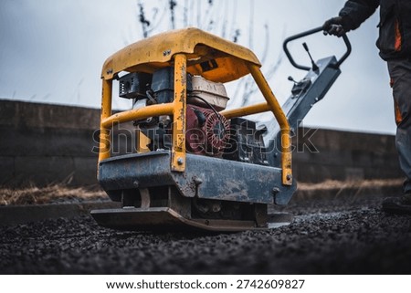 Worker working with a vibrating plate machine. Worker operates machine gravel compactor to compress gravel on construction site