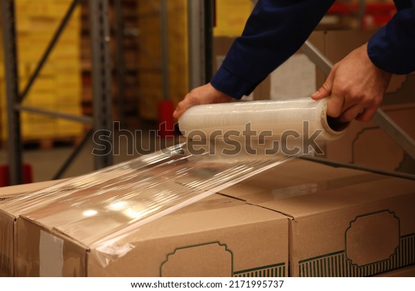 Worker wrapping boxes in stretch film at\
warehouse, closeup