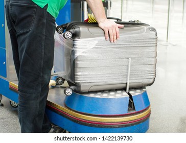 Worker Wraps Suitcase With A Transparent Film Before Travel By Airplane For Security Reason And Safety Protection From Damage. Additional Packing Of Baggage At The Airport Terminal