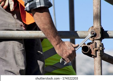 Worker with wrench in his hand builds iron scaffold on construction site  - Powered by Shutterstock