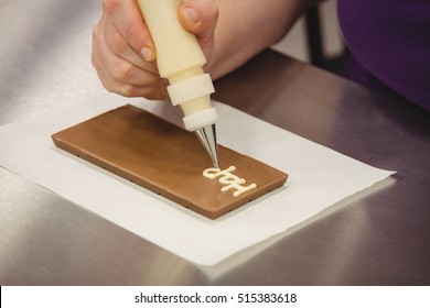 Worker writing happy birthday with piping bag on chocolate plaque in kitchen - Powered by Shutterstock