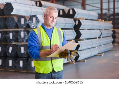 Worker writing on clipboard in front of steel tubes in warehouse - Powered by Shutterstock