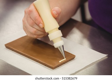 Worker writing with piping bag on chocolate plaque in kitchen - Powered by Shutterstock