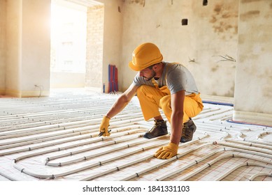 Worker In Yellow Colored Uniform Installing Underfloor Heating System.