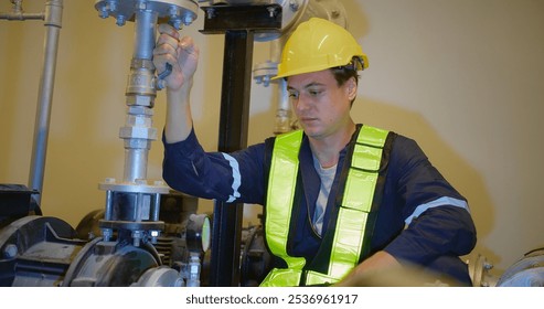 A worker in a yellow helmet and vest adjusts a pipe valve in an industrial setting, highlighting maintenance and safety within engineering environments, showcasing modern engineering practices. - Powered by Shutterstock