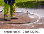 Worker in Yellow Protective Clothing Pressure Washing Monoblock Brick Paver Driveway