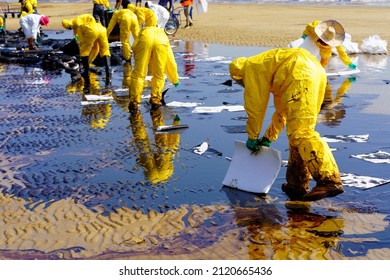 Worker in yellow quarantine suit placing oil absorbent materials to collect crude oil spill from shoreline beach. in Rayong, Thailand. (Selective Focus) - Shutterstock ID 2120665436
