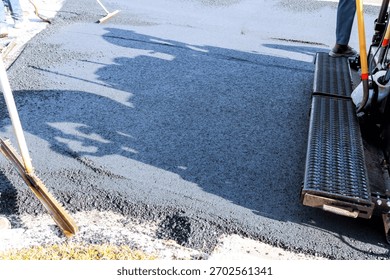 Workers apply asphalt to create smooth driveway surface during road works