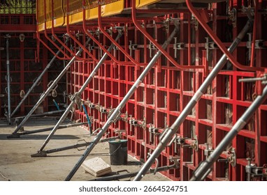 Workers are assembling concrete formwork at a construction site, using metal braces for support, ensuring stability during the building process.