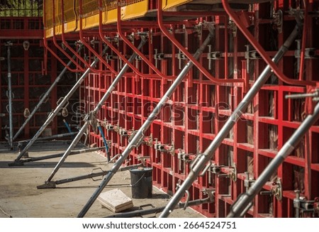 Workers are assembling concrete formwork at a construction site, using metal braces for support, ensuring stability during the building process.