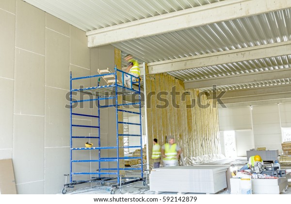 Workers are assembly gypsum wall.\
Plasterboard is under construction using mobile\
scaffolding.