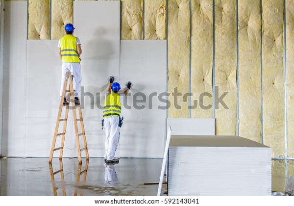 Workers are assembly gypsum wall.\
Plasterboard is under construction using wooden\
ladder.