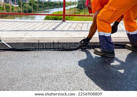 Workers attach a bitumen black tape to protect the roadside of bridge from water. Waterproofing material designed to resist and prevent water from passing through the joint placed on the pavement