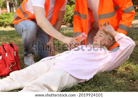 Workers with bottle of water helping mature woman in park. Suffering from heat stroke