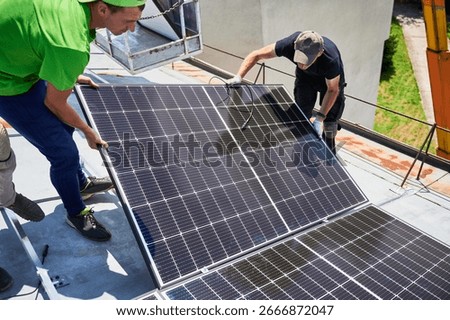 Workers building solar panel system on metal rooftop of house. Two men installers installing photovoltaic solar module outdoors. Alternative, green and renewable energy generation concept.