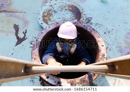 Workers climb the stairs from roof manhole of the oil tank.
