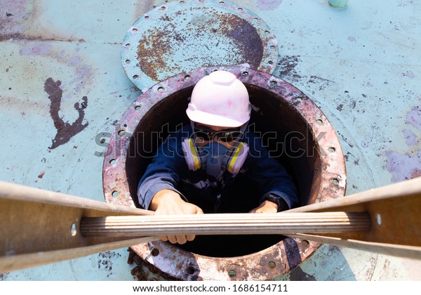 Workers climb the stairs from roof manhole of the\
oil tank.